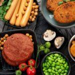 Ein Tisch voll Alternativer Proteine: Hülsenfrüchte, Pilze, Würstchen und Schnitzel aus Fleischersatz.
