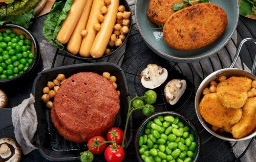 Ein Tisch voll Alternativer Proteine: Hülsenfrüchte, Pilze, Würstchen und Schnitzel aus Fleischersatz.